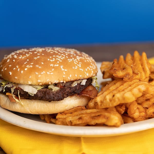 A Kirt's Drive-In burger with lettuce and sauce, served with waffle fries on a white plate.