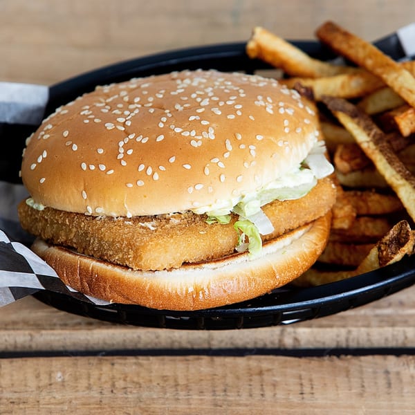 Kirt's Drive-In fish burger with lettuce and tartar sauce, served with fries in a black basket.